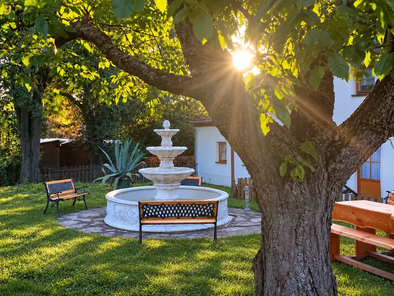 Der Springbrunnen im Garten im Abendlicht, Bänke unter dem Nussbaum